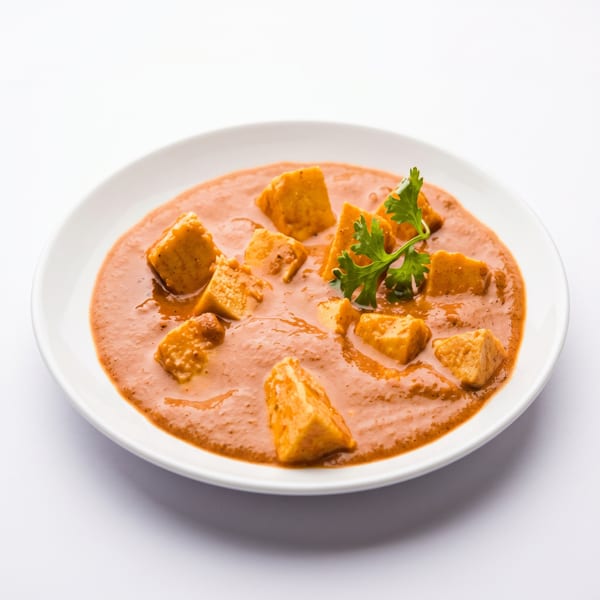 Paneer butter masala, an Indian dish with cubes of paneer in a creamy orange sauce, garnished with cilantro.