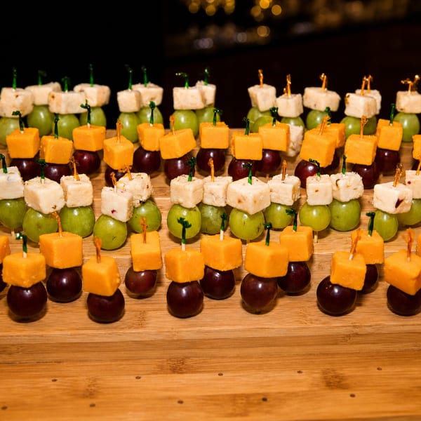 Rows of cheese and grape skewers on a tiered wooden display stand.