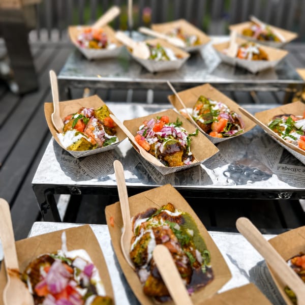 Rows of individual servings of Indian chaat in paper boats with wooden spoons.