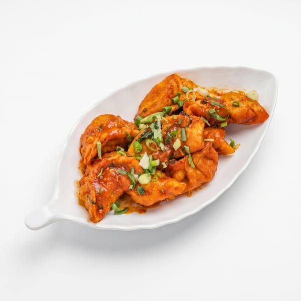 Spicy orange dumplings with green onions and herbs on a white leaf-shaped plate.