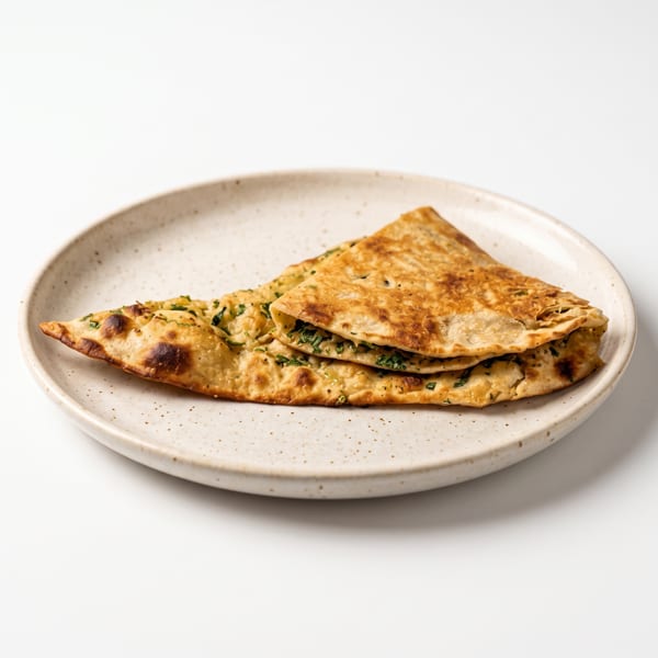 A folded flatbread filled with green herbs, served on a speckled ceramic plate.