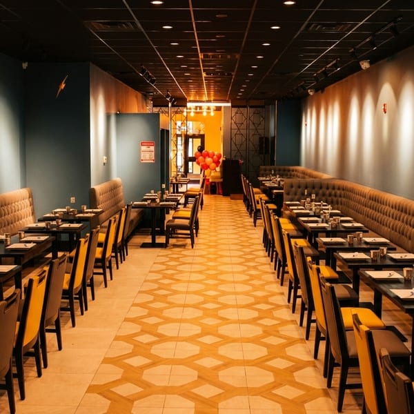 Long, narrow restaurant dining room with rows of tables, tufted banquettes, and patterned floor.