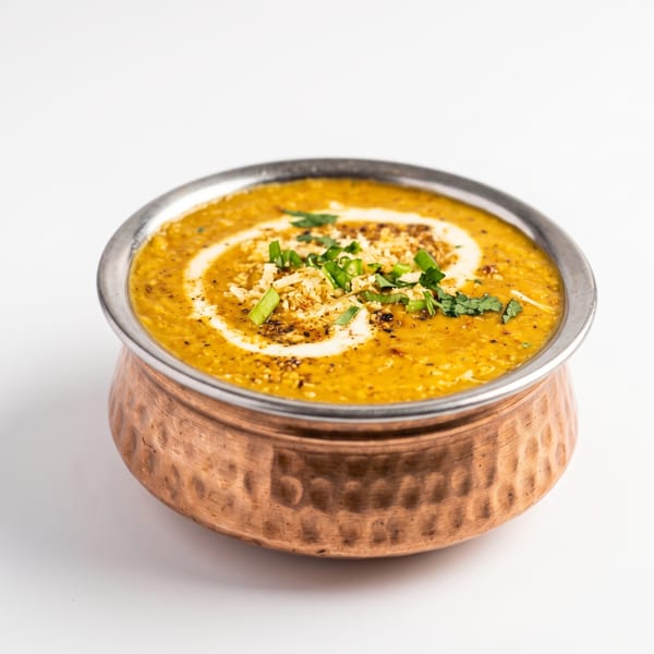 A copper bowl filled with yellow dal, garnished with cream, herbs, and spices.