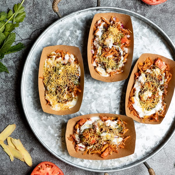 Four servings of Indian street food chaat in paper trays on a metal platter.