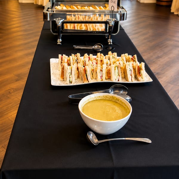 A buffet table with a chafing dish of bread, a platter of sandwiches, and a bowl of soup.